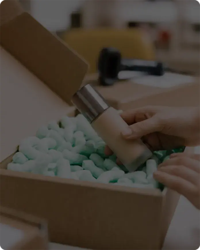 Worker packing an unbranded cosmetic container into a shipping box
