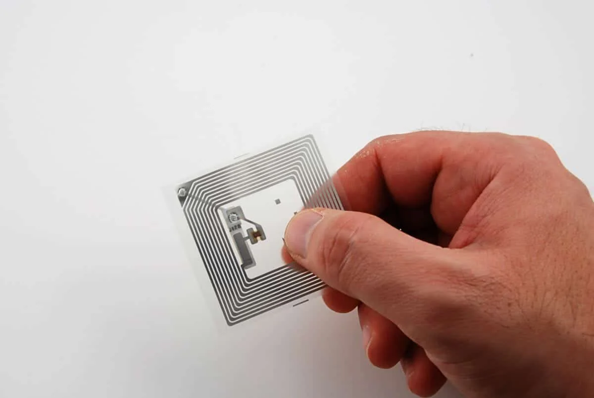 Hand holding an unbranded NFC inlay showing the printed antenna and chip