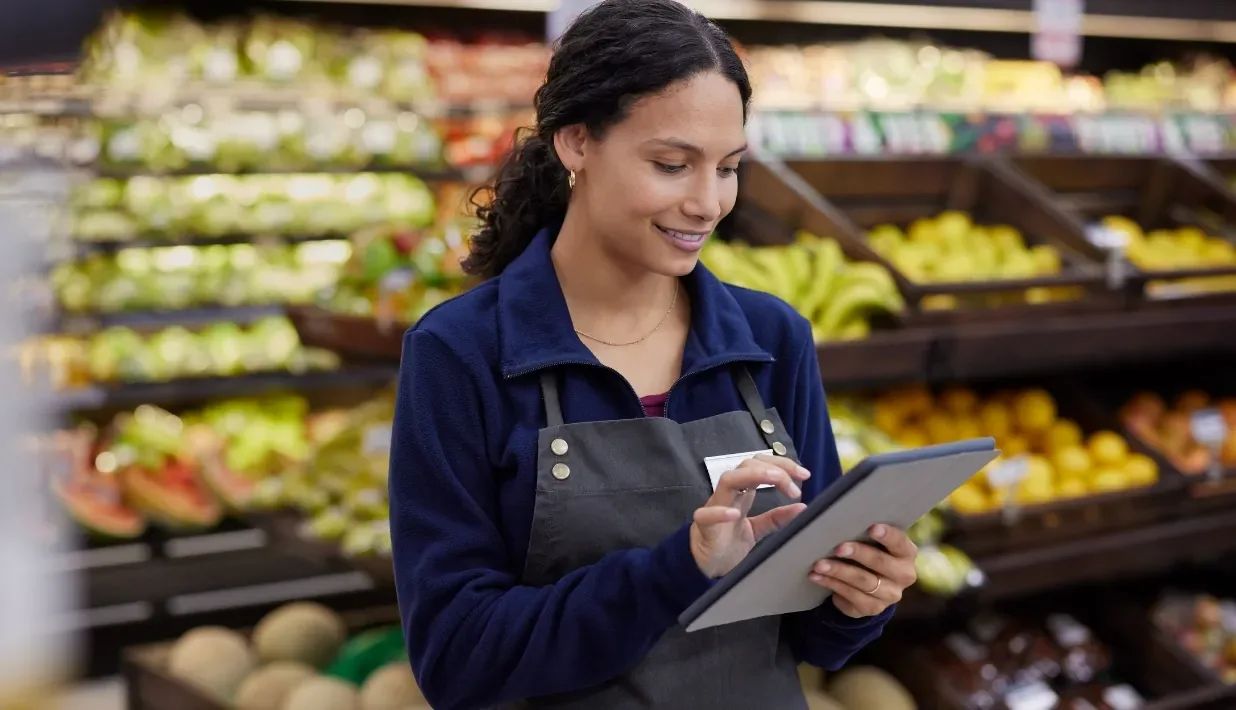 Store team member checking inventory with a tablet in a produce aisle